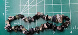 May include: A strand of black, white, and gray gemstone beads. The beads are irregularly shaped and have a natural, tumbled look. The beads are strung on a clear elastic cord 