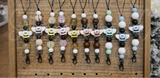 Bee-themed freshie hangers with colorful beads on a wooden pegboard.