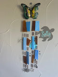 A brown and blue stained glass wind chime with metal charms, butterfly-shaped glass pieces, and a monofilament fishing cord.