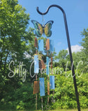 Butterfly wind chime with colorful hanging elements on a metal hook against a natural background.