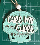 May include: A teal seashell-shaped wooden ornament with the text "Call me on my shell I'll be at the beach" in brown lettering.