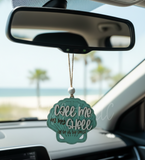 "Teal seashell wooden car charm with 'Call me on my shell' text hanging from a car rearview mirror with beach and palm tree background."