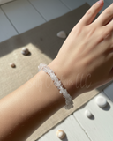 Hand wearing a clear beaded bracelet on a light background
