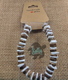 A handmade bracelet with coconut and puka shell beads, displayed on a textured background.