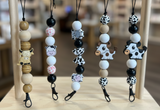 Set of cow-themed lanyards with beads on a wooden stand.