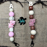 Two handmade freshie hangers with silicone beads and a pig design, laid out on a burlap fabric surface.