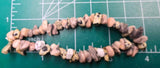 May include: A bracelet made of irregular, light brown and gray stone beads. The beads have black speckles and are strung together to form a circular shape. The bracelet is approximately 7 inches in circumference.