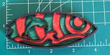 A colorful wooden magnet shaped like a dolphin surfboard with a vibrant green-and-orange design, placed on a measuring mat surface.