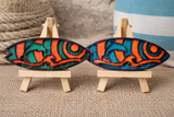 Two colorful wooden surfboard-shaped magnets on small wooden stands with a textured background.