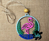 A wooden car charm with a flamingo design, pink, green, and blue colors, with a string for hanging.