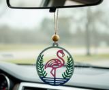 Car air freshener with flamingo design hanging from a car's rearview mirror.
