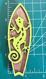 A magnet shaped like a green gecko mounted on a brown surfboard-shaped magnet on a measuring mat.
