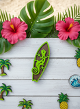 Decorative magnets with a lizard on a surfboard, surrounded by tropical flowers and plants on a wooden surface.