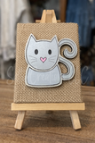Decorative cat-shaped mug on a burlap background with a wooden stand.