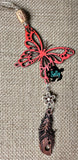 May include: A red wooden butterfly charm with a brown wooden feather and a white wooden flower charm hanging from a tan cord. 