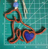 Handmade wooden dog silhouette car charm with a blue heart inlay, and blue acyrlic bead on a measuring mat background