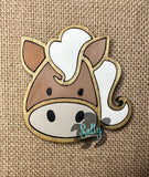 A wooden magnet shaped like a horse with a white and brown color scheme, placed on a burlap background.