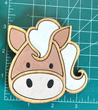 A wooden magnet shaped like a horse with a white and brown color scheme, placed on a measuring mat background.