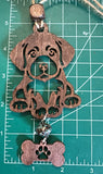 May include: A wooden dog ornament with a brown finish. The dog is sitting  and has a bone tag hanging from its feet. The bone has a paw print cut out of it. With a measuring mat as the background