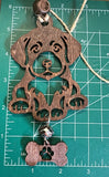 May include: A wooden dog ornament with a brown finish. The dog is sitting  and has a bone tag hanging from its feet. The bone has a paw print cut out of it. With a measuring mat as the background