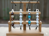 Set of keychains with beads on a wooden display stand outdoors.
