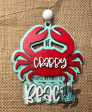 A wooden car charm with a red crab design and the text 'IF CRABBY PLEASE RETURN TO BEACH'.