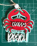 May include: A wooden crab ornament with the text "If Crappy Please Return To Beach" in white lettering on a teal measuring background. The crab is red 