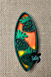 A decorative surfboard-shaped object with leaf patterns on a plain burlap background.