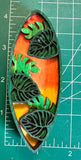 A decorative surfboard-shaped object with leaf patterns on a measuring mat background.