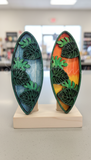 Two decorative surfboard-shaped objects with leaf patterns on a plain background