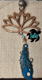 A wooden car charm with a lotus flower design, featuring hanging blue wooden feather and strings and a small beaded ornament.