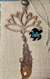 A wooden car charm with a lotus flower design, featuring hanging brown wooden feather and strings and a small beaded ornament.