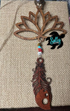 A wooden car charm with a lotus flower design, featuring hanging dark brown wooden feather and strings and a small beaded ornament.