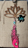 A wooden car charm with a lotus flower design, featuring hanging pink wooden feather and strings and a small beaded ornament.