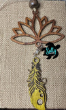 A wooden car charm with a lotus flower design, featuring hanging yellow wooden feather and strings and a small beaded ornament.