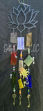 Close-up of a lotus flower wind chime featuring vibrant chakra-colored glass panes, iridescent beads, and metal charms including a sun, cross, and seahorse key hanging against a dark backdrop