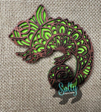 A green and brown tribal-style chameleon magnet made from wood.