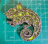 A green and brown tribal-style chameleon magnet made from wood on a measuring mat. 