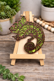 Decorative wooden lizard on a small easel with plants in the background