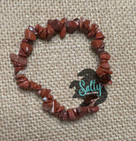 A bracelet made with red jasper stones, displayed on a textured background.