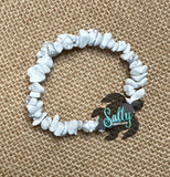 May include: White howlite chip bracelet. The bracelet is made of small, irregular shaped white stones with gray veining. The bracelet is on a burlap background.