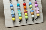 Colorful bead freshie hangers with boat shapes on a wooden board.