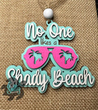 A wooden car charm with a string, featuring text and a graphic of sunglasses on a burlap background.