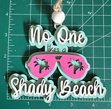 A wooden car charm with a string, featuring text and a graphic of sunglasses on a measuring mat background.