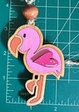A pink wooden flamingo ornament with a brown wooden bead at the top. The flamingo has a pink body, orange beak, and white eyes. The ornament is about 3 inches tall.