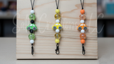 Three colorful bead keychains on a wooden block with a blurred background.