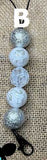 Silver beaded freshie hanger with decorative patterns on a textured beige background