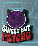 Purple glittery face with black horns and red text 'Sweet But Psycho' on a gray cutting mat.