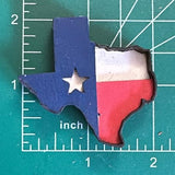 A magnet shaped like the Texas flag, with blue, white, and red colors, placed on a measuring mat background.