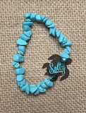 A turquoise bracelet with a mix of smooth and rough stones, featuring a black logo on a textured background.